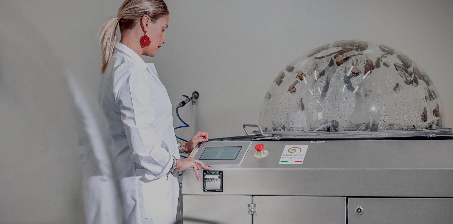 An operator in a white coat uses the touch panel of a Muller extractor; snails are visible inside the domes.