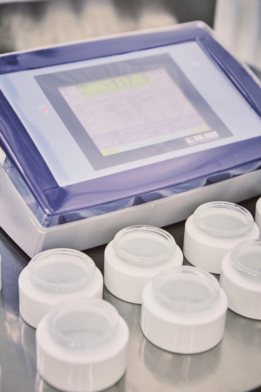 Cosmetic jars lined up beside a measuring instrument.